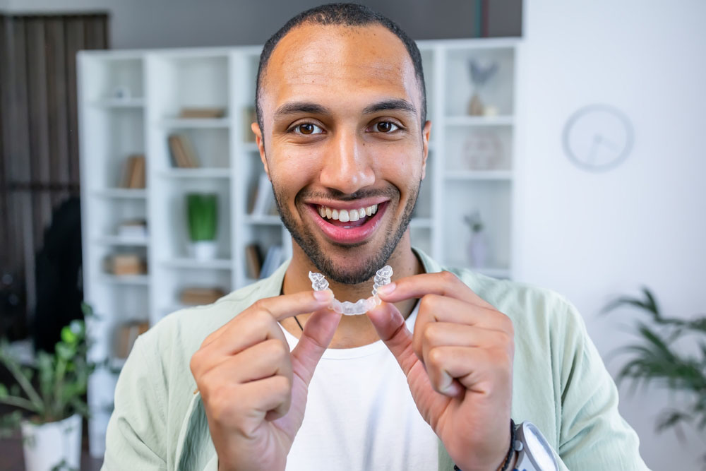 Man holding Invisalign clear aligners with confident healthy smile in Flint, MI