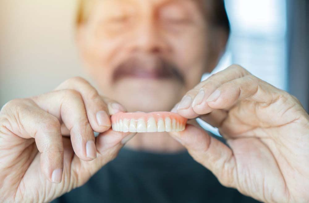 Patient holding custom dentures after restorative dental treatment, TrueDent Dentures in Southfield, MI