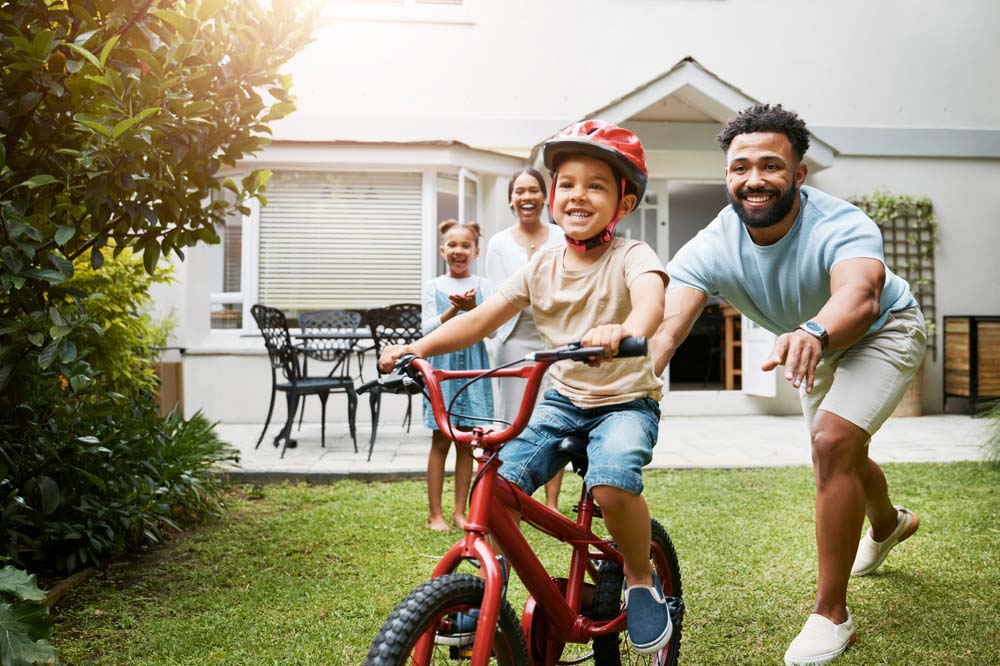 Child riding bicycle with family smiling and healthy happy smiles after Emergency Dentistry in Flint, MI