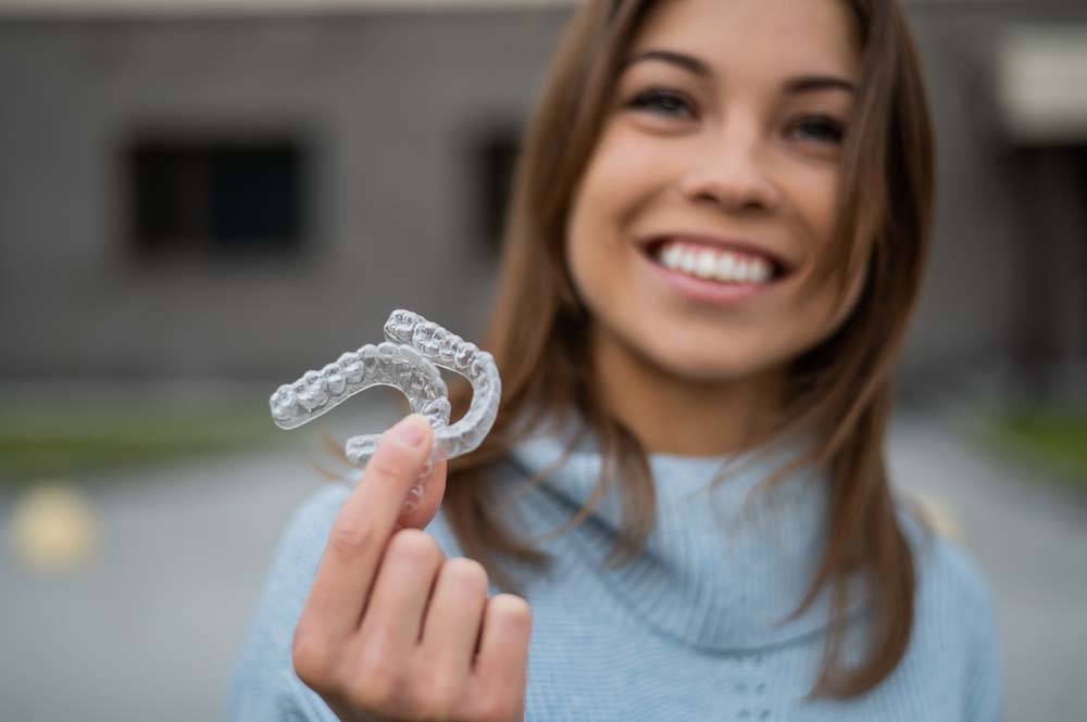 Woman holding clear aligners for Invisalign teeth straightening treatment in Livonia, MI